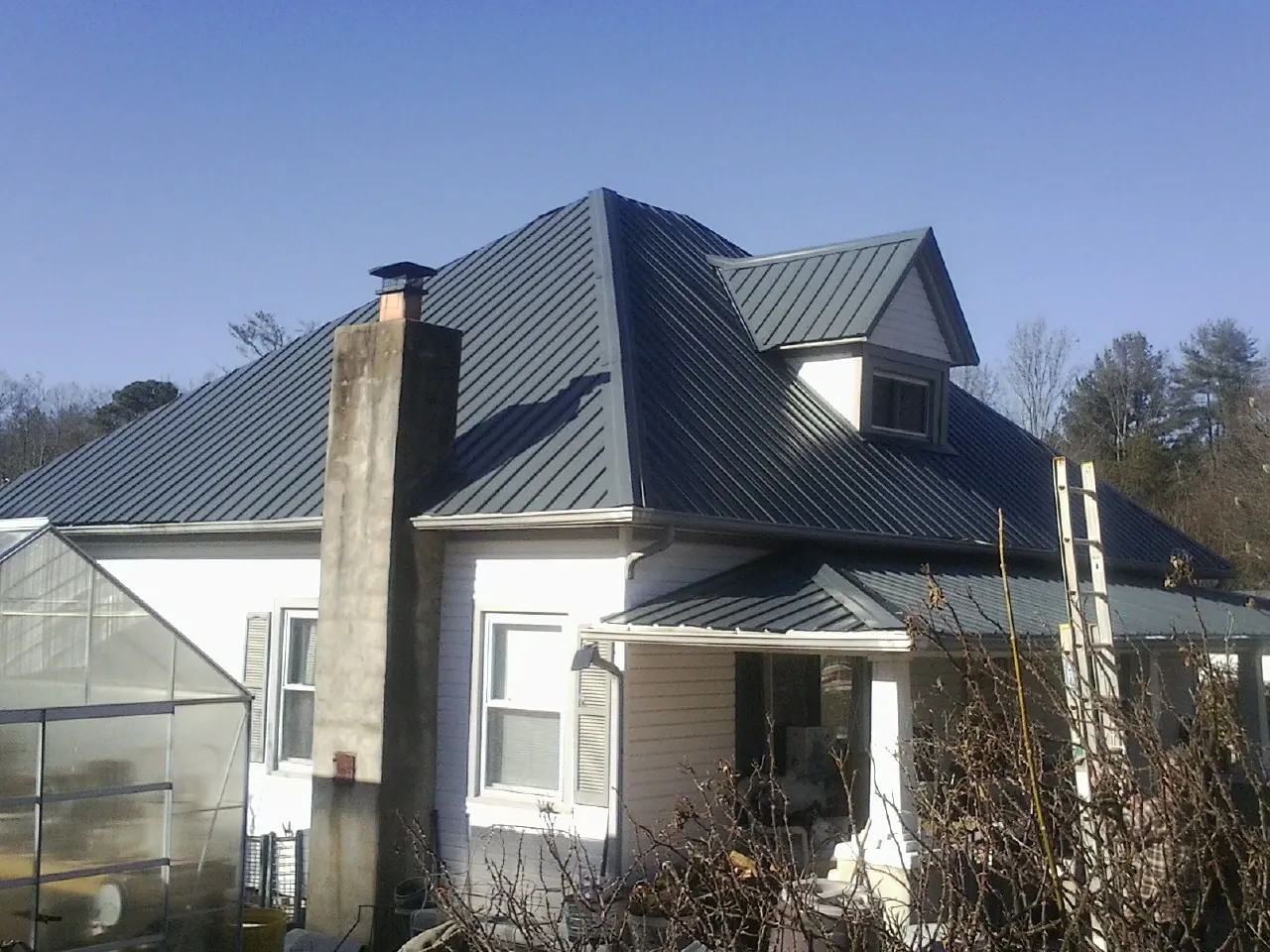 Dark blue standing seam metal roof on a white farmhouse with dormer — Slate & Tile Roof Repair by Roofing Brothers in Owasso