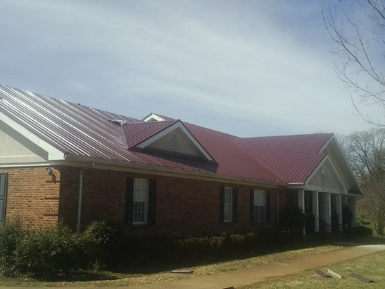 Red metal roof with gabled entries on a long brick building, from a Hail Damage Roof Repair job in Owasso