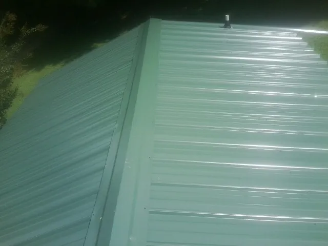 New green metal panels meeting at the ridge of a roof — Flat Roof Repair work by our crew in Owasso