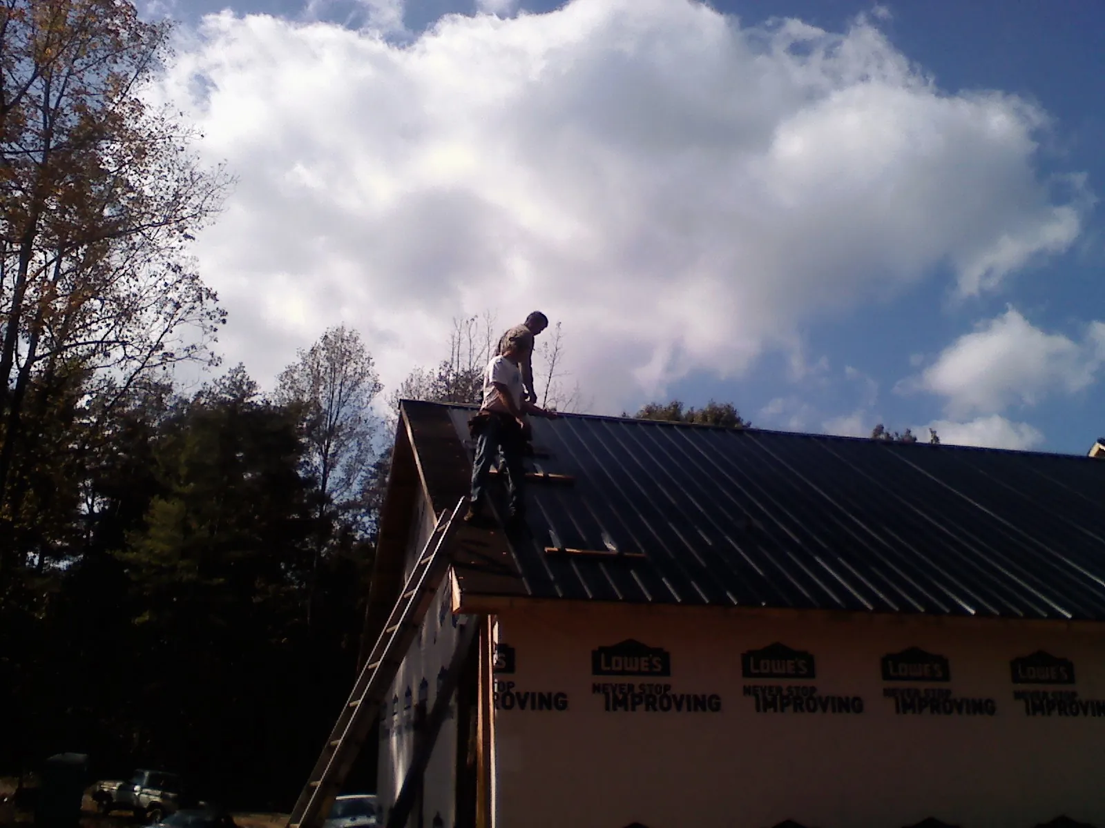 Roofer fastening dark metal panels high against a cloudy sky, from a Roof Inspection job in Owasso