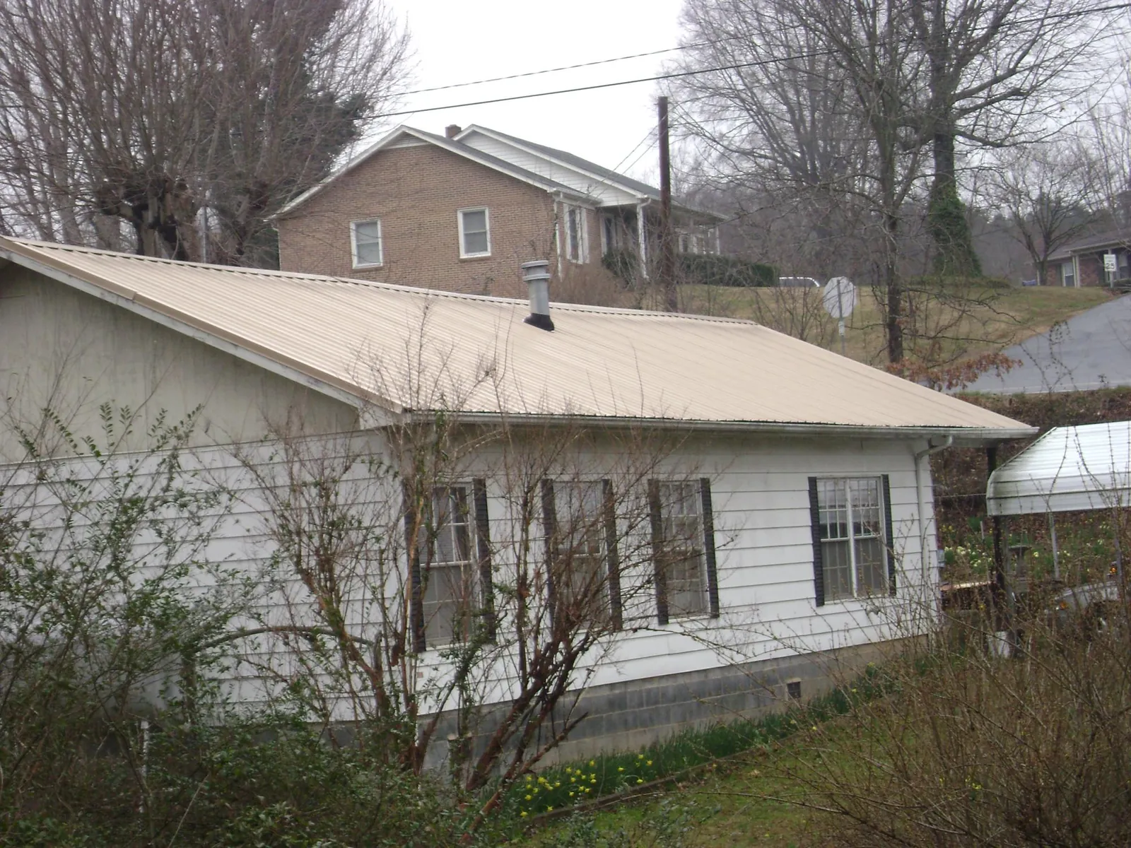 Tan metal roof on a white sided house set into a hillside — Commercial Roofing by Roofing Brothers in Owasso